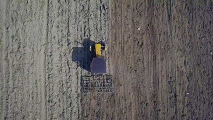 A farmer on a red tractor with a seeder sows grain in plowed land in a private field in the village area. Mechanization of spring field work. Farmer's everyday life. Processing of land. The agrarian.