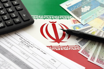 Iranian annual income tax return form F20-25-006 ready to fill on table with pen, calculator and iranian money on flag close up