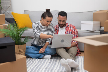 Couple sits on floor among unpacked boxes together choose wallpapers for new kitchen from web site...