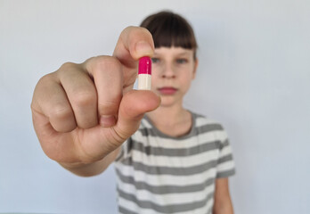 Little girl with vitamin tablet on light background