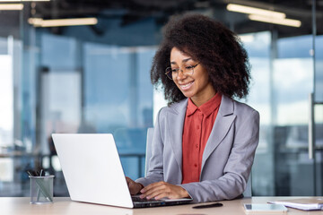 Young smiling African American female student studying on campus at desk using laptop.