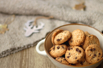 Bowl of cookies, cup of tea, dry oranges, pine cones, books, reading glasses, small presents, various Christmas decorations and lit candles on the table. Cozy Christmas hygge. Selective focus.