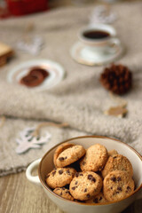 Bowl of cookies, cup of tea, dry oranges, pine cones, books, reading glasses, small presents, various Christmas decorations and lit candles on the table. Cozy Christmas hygge. Selective focus.