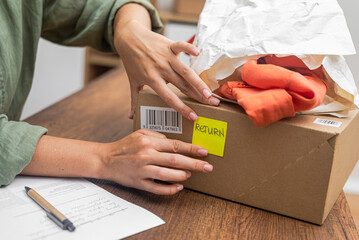 woman online shopper affixes a barcode sticker to a cardboard box, marking it for return and refund.  - obrazy, fototapety, plakaty