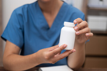 close up pharmacist In a clinic setting, doctor, dressed in blue, holding a jar of pills while discussing treatment. 