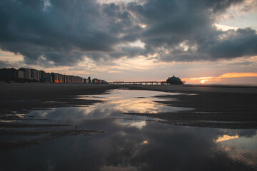 Obraz premium Sunset on the sandy beaches of Oostende, western Belgium. The last rays of the sun are breaking through the clouds. Red-orange hell
