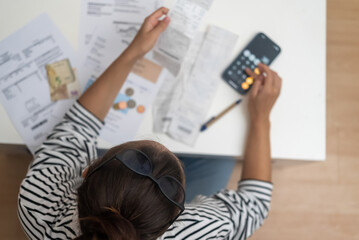 Focused woman counts utility bank bills with calculator of smartphone sitting at desk with documents female works in office of accommodation upper view