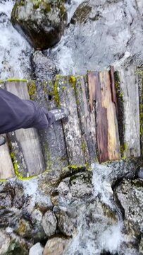 Slow motion 4K video POV view of Man's legs in trekking boots crossing mountain creek by wooden bridge during Makalu Barun National Park trek in Nepal. Mountain hiking and active people concept image.