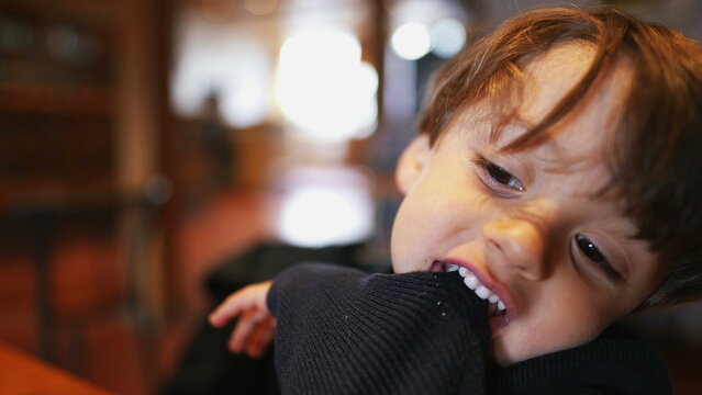 Bored small boy pulling sleeve with teeth and mouth while seated at restaurant with nothing to do. Child bites sweater feeling boredom