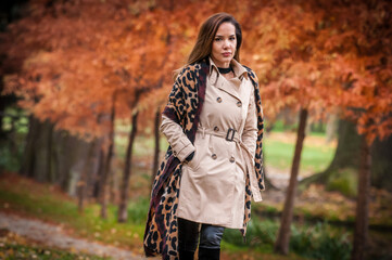 young girl in coat in forest. Fashion woman in coat in park. Slim young fashion model wearing white coat outdoor. Beautiful woman in leopard coat  in the autumn park