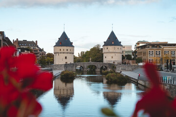 Fototapeta na wymiar Kortrijk town centre with two historic towers on the riverside. Flowers, river and historic buildings. Belgian city in the south of the country
