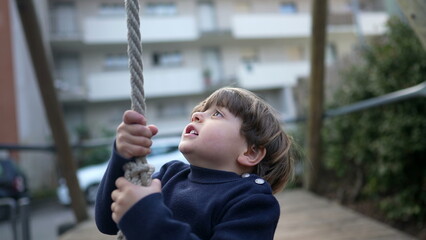 Obraz premium Child Gripping Wire Slide Rope at Public Park During Autumn Season. Heartwarming Close-Up of Joyful Child Sliding on Wire Rope Between Trees, Nostalgic Park Fun