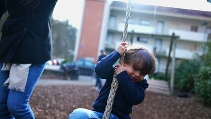 Obraz premium Child holding into wire slide at public park during autumn fall season. Kid gripping rope in daylight