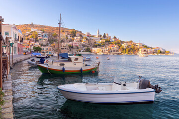 Colorful traditional multi-colored houses and boats at the pier on the shore of the bay on Symi island.