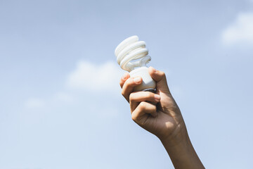 Recyclable electric waste held in hand up on sky background. Hand holding light bulb for recycle...