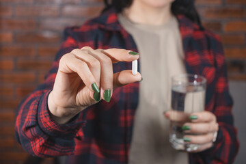 Young woman taking medicine, white pill and holds in a hand glass of water, close-up view