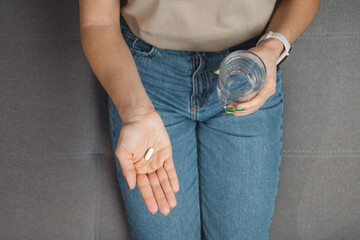Young woman takes a medicine, white pill and holds in a hand glass of water, close-up view - obrazy, fototapety, plakaty