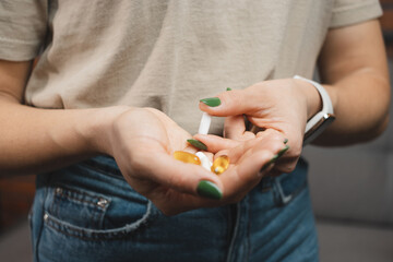 Young woman takes one white medical pill and holds in a hand pile of various pills and capsules, close-up view