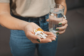 Young woman holds various medical pills and capsules in a hand and glass of water, close-up view