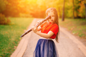Young attractive girl playing clarinet, ebony in fall park