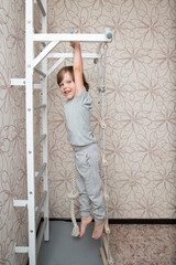 Little kid climbing a ladder in an apartment, a boy playing on a white wall bar