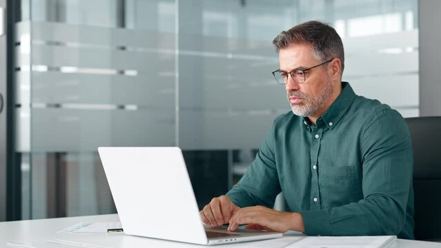Busy middle aged professional business man executive investor using computer working at desk. Male manager expert looking at laptop thinking on online finance market analysis, elearning in office.