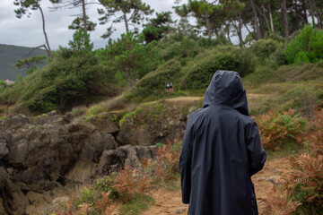 Young woman dressed with a dark blue raincoat walking on the mountains. She has the hood of the coat on. Rainy winter day.