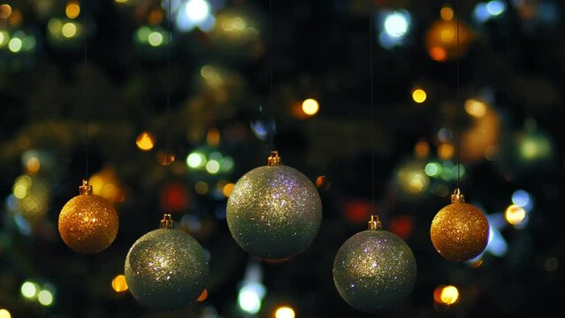 Golden and silver spinning balls against the background of glowing Christmas garlands on a Christmas tree in blur. Medium plan