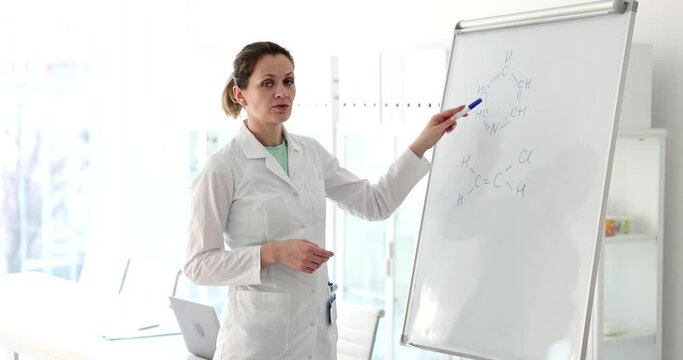 Female scientist teacher writes and explains formula on white board in laboratory. Chemical formulas of substances