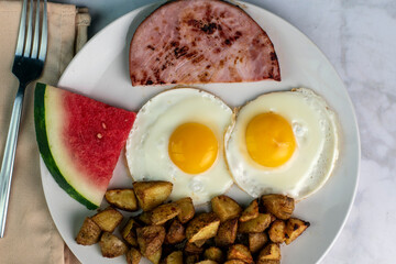tw0 fried eggs with home fries and  ham