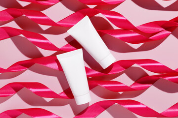 Blank white plastic cosmetic tubes with pink ribbons on pink background. Cosmetic beauty product...