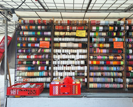 Verkaufswagen mit reicher Auswahl an Geschenkb&auml;ndern, aufgereiht &uuml;bersichtlich ausgestellt. Verschiedene Farben, schmal bis breit, einfarbig bis zu Weihnachtsmustern.  2 rote Boxen mit breiten B&auml;ndern