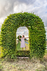 A woman with balloons is standing in an arch made of green leaves