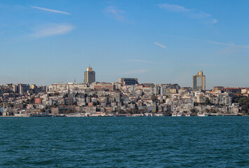Fototapeta premium Istanbul's skyline from the Bosphorus: sunny, with a mix of skyscrapers, historic buildings, and several boats on the calm blue water.