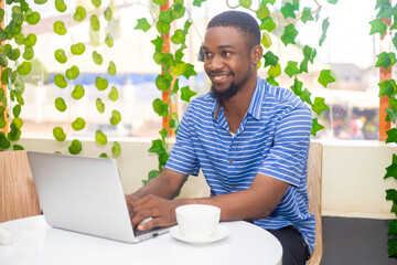 Smiling young africa business man using laptop sitting outdoor