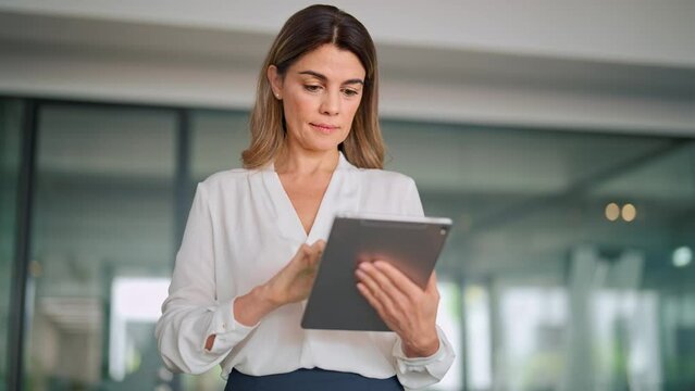 Mature busy latin business woman financial manager using digital tablet working in office. Middle aged professional businesswoman executive holding tab technology device standing at work.