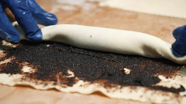 The baker twists the raw dough with poppy seeds to prepare the pastry. Close-up shooting. Making buns with poppy seeds