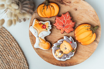 Set of autumn style gingerbread cookies with festive icing in the shape of hedgehog, fallen leaves, fox and pumpkin on the wooden background.