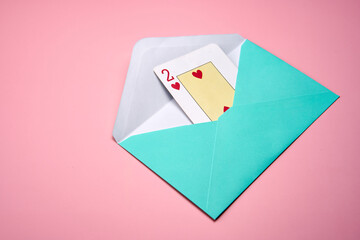 Two hearts playing card inside a blue envelope on a pink background. Concept of love.