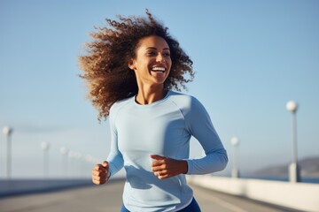 Young afro american woman runner running on city bridge road against blue background