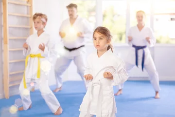 Foto op Aluminium In gym, family of four repeats movements of karate card and practicing kicks and punches in unison, is intently preparing for sparring. © JackF