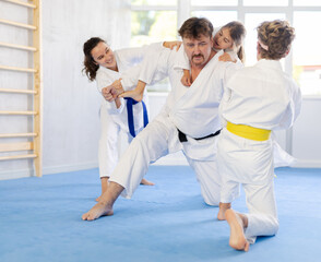 Fototapeta na wymiar During martial arts training, father of family repels attack of whole family. Parents and children have fun in gym after workout