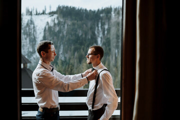 A respectful father helps his mature son put on a bow tie before the wedding. Shooting in the hotel...