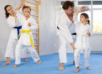 Children with parents practicing judo together on sports mats in gym