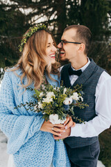 winter wedding in the mountains. Portrait of a happy and smiling bride and groom against the background of a winter forest. Beautiful bride and groom tenderly embrace. Modern winter wedding.