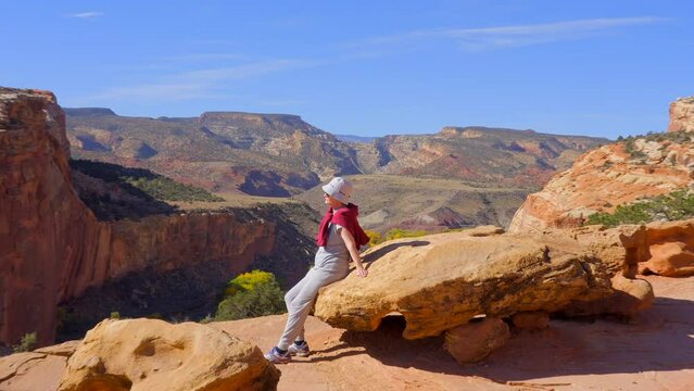 Establishing shot of female tourist at mountain trail with red rocks background in Hickman Natural Bridge Trail, Capital Reef National Park, Utah, North America. Day time on October 2023. Still camera