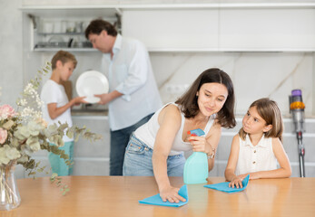 Fototapeta premium Joyful family with two children doing cleaning in kitchen in apartment