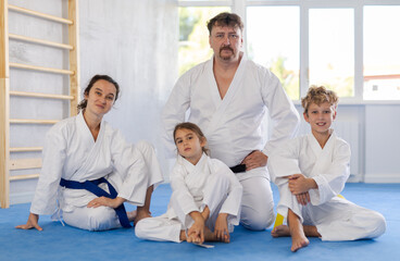 Married couple and their children in white kimono sitting on knees on tatami in gym