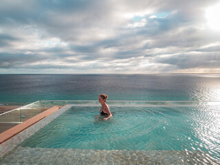 Portrait of a woman standing in an infinity pool looking over the sea