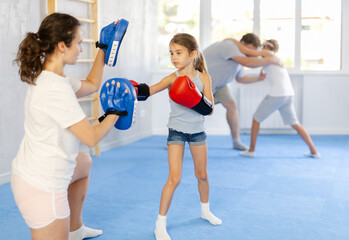 Skinny little determined girl in boxing gloves training with mother during self-defense course,...